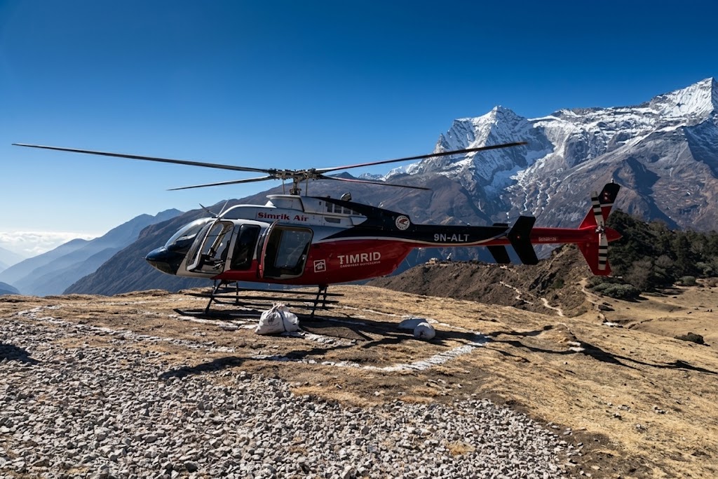 Helicopter resting on a mountain ridge landing site during a scenic Everest base camp tour under a clear blue sky.
